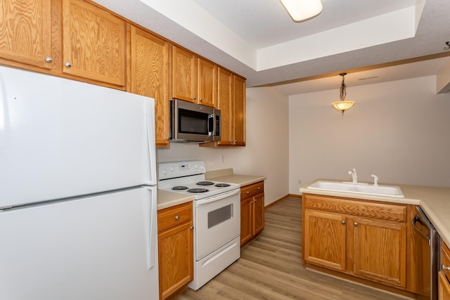 kitchen featuring stainless steel appliances, hanging light fixtures, sink, and light hardwood / wood-style flooring