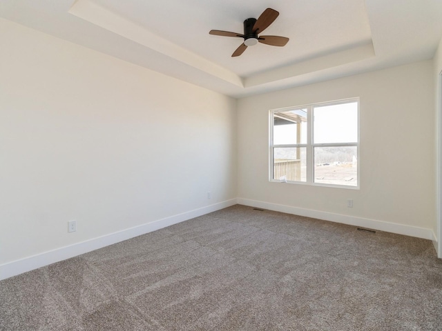 empty room featuring visible vents, baseboards, ceiling fan, carpet floors, and a raised ceiling