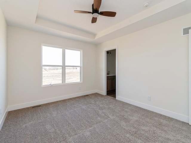 carpeted spare room featuring visible vents, baseboards, a tray ceiling, and ceiling fan