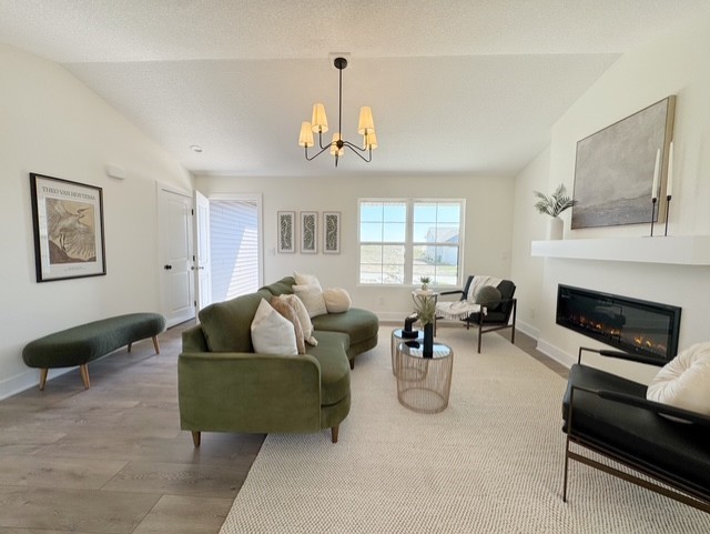 living room featuring a glass covered fireplace, vaulted ceiling, baseboards, and a notable chandelier