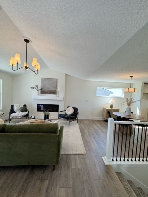 living area with vaulted ceiling, a textured ceiling, a glass covered fireplace, a notable chandelier, and dark wood-style floors