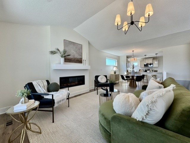 living area featuring vaulted ceiling, visible vents, baseboards, a glass covered fireplace, and a notable chandelier