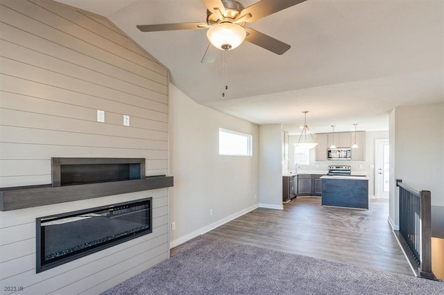 unfurnished living room with lofted ceiling, sink, ceiling fan, a large fireplace, and dark hardwood / wood-style flooring