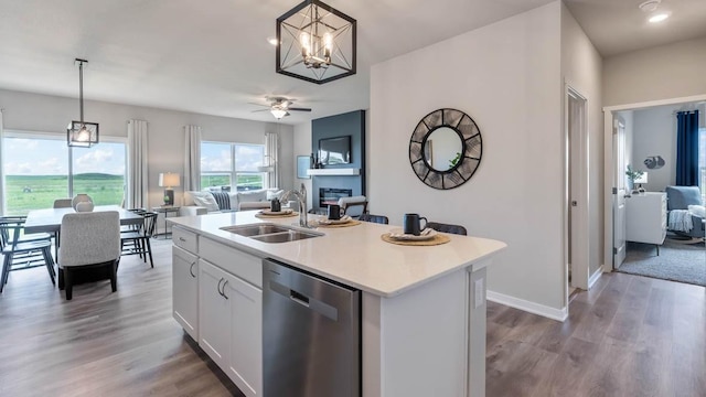 kitchen with stainless steel dishwasher, a glass covered fireplace, open floor plan, white cabinetry, and a sink