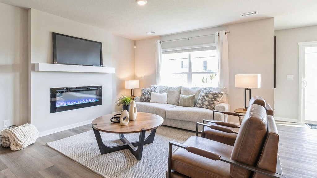 425 Kinley Dr, Waukee, IA 50263 - living room featuring a glass covered fireplace, wood finished floors, visible vents, and baseboards