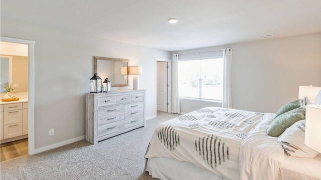 bedroom featuring baseboards, ensuite bathroom, and light colored carpet