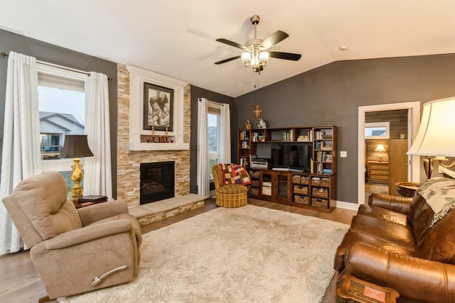 living room with ceiling fan, a stone fireplace, wood-type flooring, and vaulted ceiling