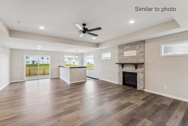 unfurnished living room with ceiling fan with notable chandelier, dark hardwood / wood-style flooring, and a stone fireplace