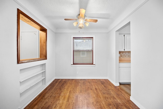 spare room featuring built in shelves, ceiling fan, light wood-type flooring, and a textured ceiling