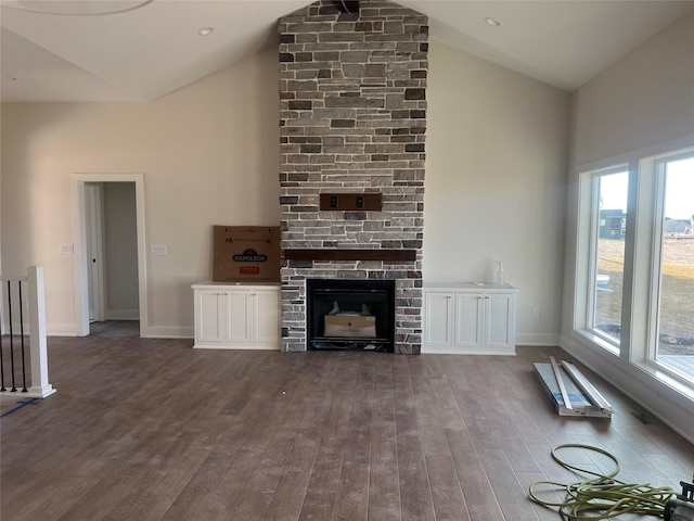 unfurnished living room featuring a stone fireplace, dark wood-style floors, baseboards, and high vaulted ceiling