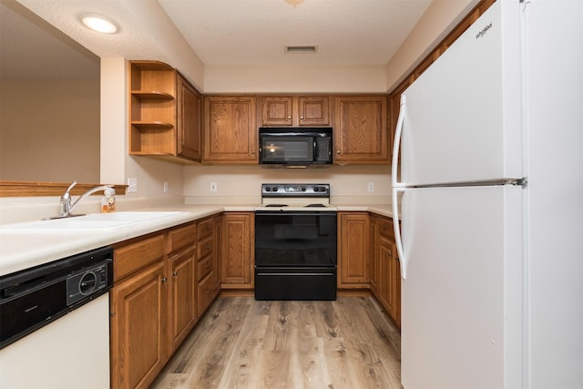 kitchen with black appliances, sink, light wood-type flooring, and a textured ceiling