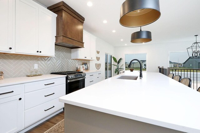 kitchen with decorative backsplash, sink, stainless steel range oven, white cabinetry, and an island with sink