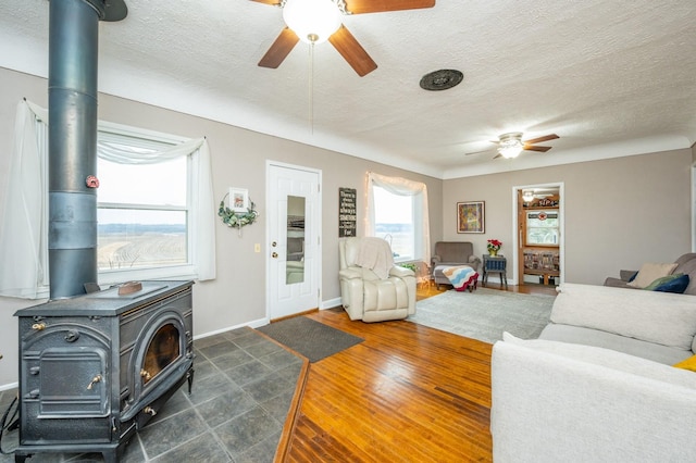 living room with ceiling fan, a wood stove, and a textured ceiling