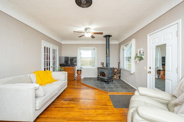 living room featuring ceiling fan, a wood stove, hardwood / wood-style floors, and a textured ceiling