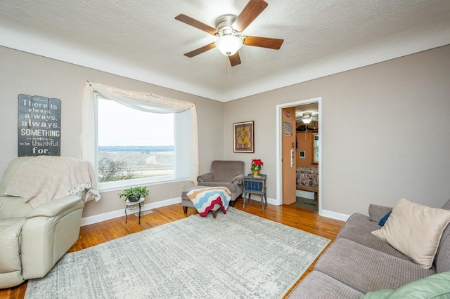 living room with ceiling fan, light wood-type flooring, and a textured ceiling