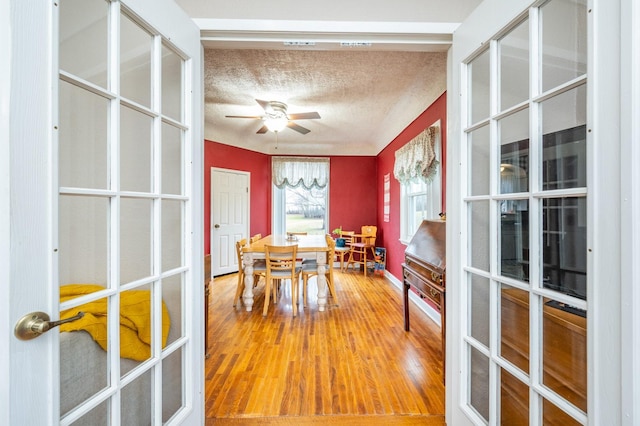 dining space with a textured ceiling, ceiling fan, wood-type flooring, and french doors