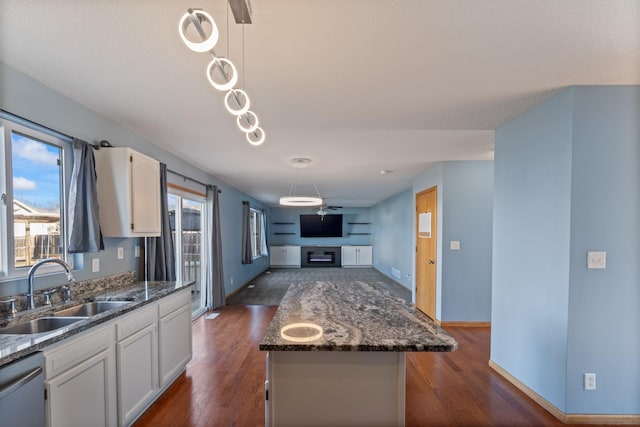 kitchen featuring dark wood-type flooring, stainless steel dishwasher, a glass covered fireplace, white cabinets, and a sink