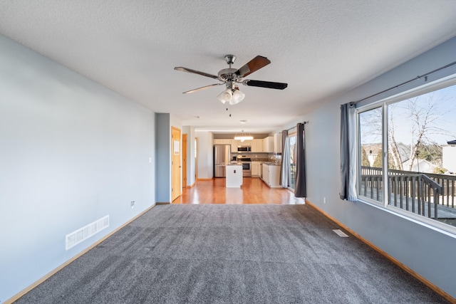 unfurnished living room featuring visible vents, ceiling fan, a textured ceiling, and baseboards