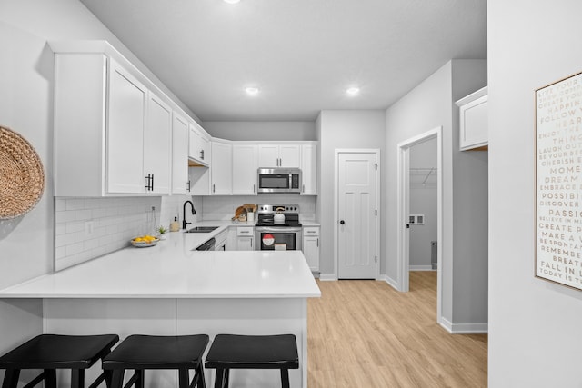 kitchen featuring kitchen peninsula, backsplash, stainless steel appliances, white cabinets, and a breakfast bar area