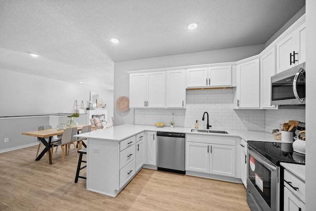 kitchen with white cabinets, sink, appliances with stainless steel finishes, a kitchen bar, and kitchen peninsula