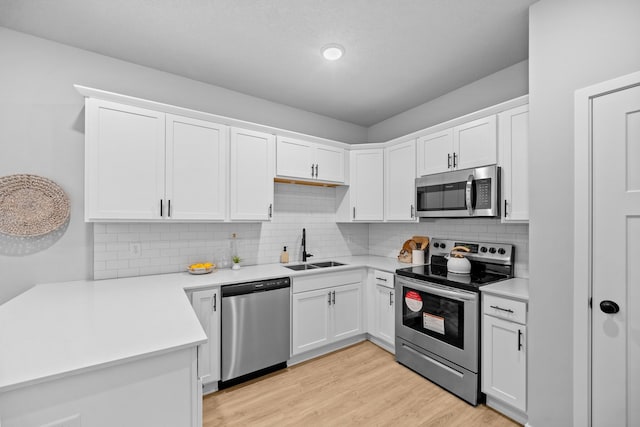 kitchen with appliances with stainless steel finishes, backsplash, light wood-type flooring, sink, and white cabinets