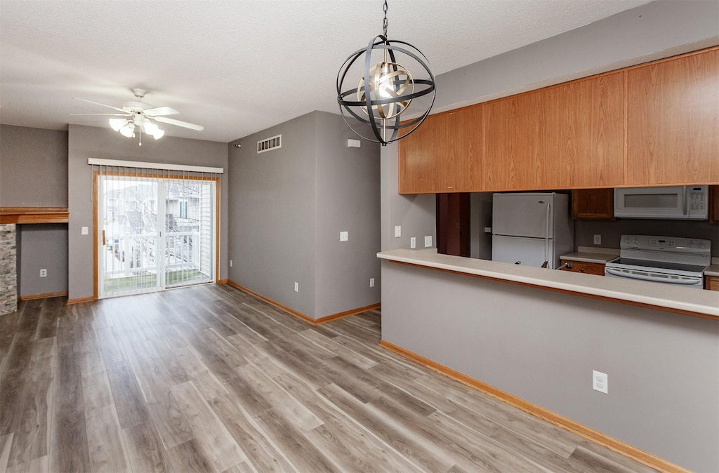 kitchen with hanging light fixtures, ceiling fan with notable chandelier, white appliances, and light hardwood / wood-style flooring