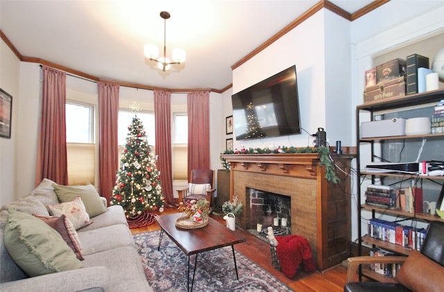 living room with wood-type flooring, a brick fireplace, ornamental molding, and a notable chandelier