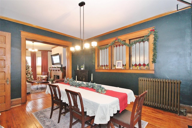 dining room with hardwood / wood-style flooring, crown molding, radiator, and a chandelier