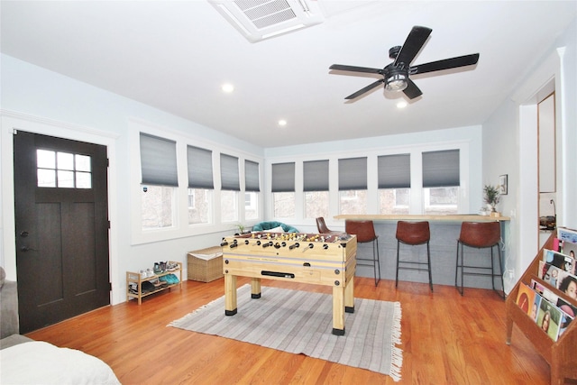 rec room with bar, light hardwood / wood-style floors, and ceiling fan