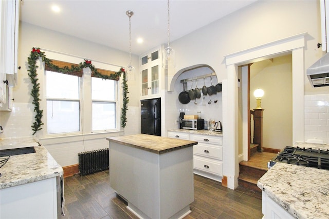 kitchen with black refrigerator, backsplash, radiator, a kitchen island, and white cabinetry