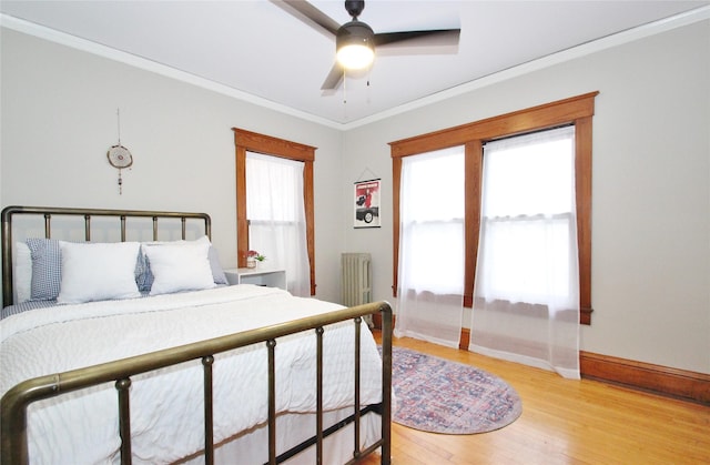 bedroom featuring light wood-type flooring, ornamental molding, a ceiling fan, radiator heating unit, and baseboards