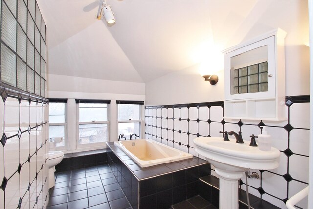 bathroom featuring lofted ceiling, tile patterned floors, toilet, tile walls, and tiled tub