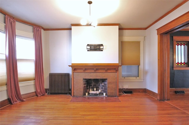 unfurnished living room with crown molding, a brick fireplace, radiator heating unit, and wood finished floors