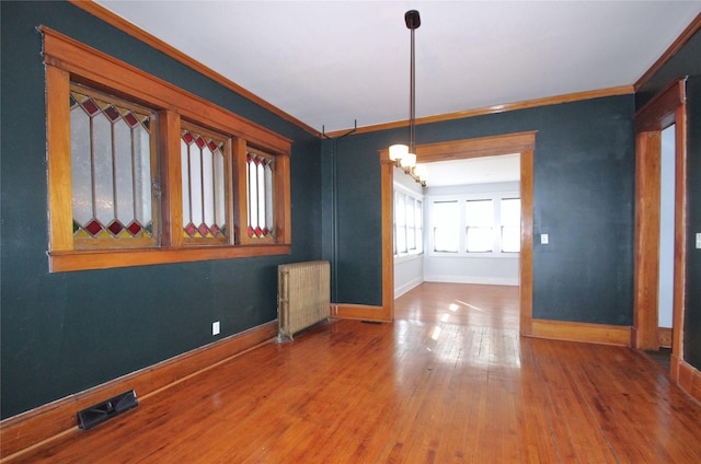 empty room with visible vents, wood finished floors, ornamental molding, and radiator heating unit