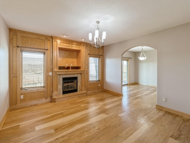 unfurnished living room featuring a fireplace, a textured ceiling, light wood-type flooring, and a notable chandelier