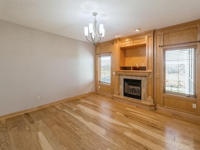 unfurnished living room featuring light hardwood / wood-style flooring, a tile fireplace, and a chandelier