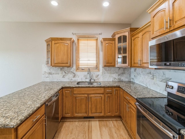 kitchen with stone countertops, stainless steel appliances, light hardwood / wood-style flooring, and sink