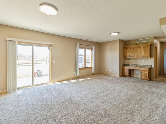 unfurnished living room with built in desk, light colored carpet, and plenty of natural light