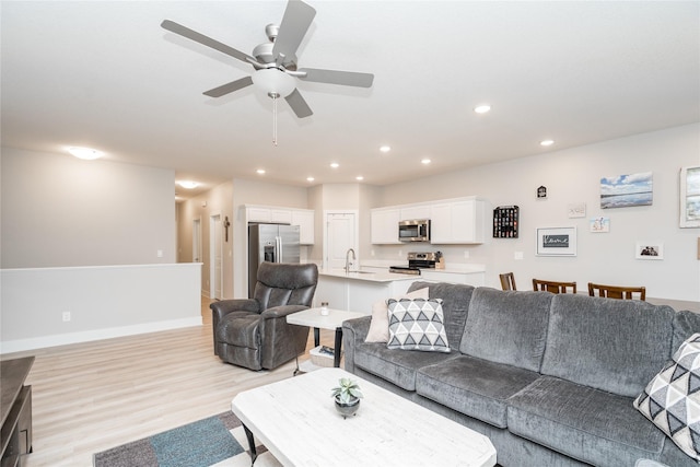 living room featuring light hardwood / wood-style flooring, ceiling fan, and sink