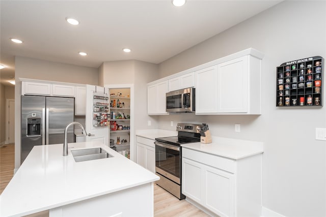 kitchen featuring a center island with sink, white cabinets, sink, light wood-type flooring, and stainless steel appliances