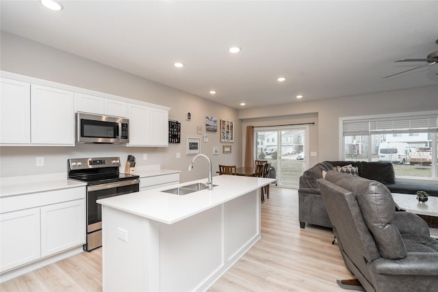 kitchen with a kitchen island with sink, sink, light wood-type flooring, white cabinetry, and stainless steel appliances