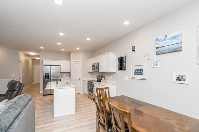 kitchen with stainless steel appliances, white cabinetry, a kitchen island with sink, and light hardwood / wood-style flooring