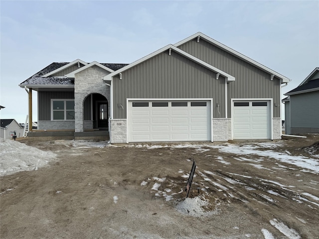 view of front of property featuring a garage, stone siding, and roof with shingles