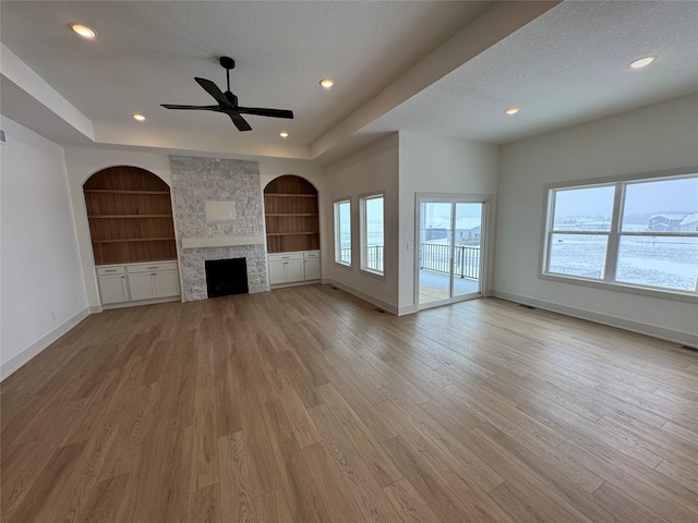 unfurnished living room featuring built in shelves, a stone fireplace, light wood finished floors, and a textured ceiling