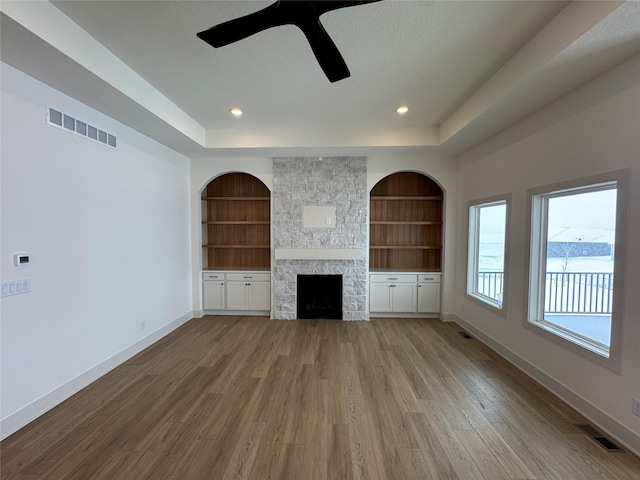 unfurnished living room with a tray ceiling, a fireplace, visible vents, and baseboards