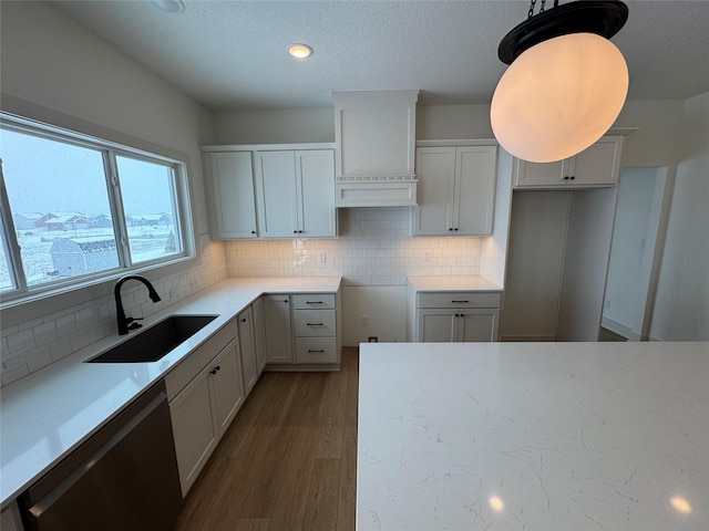 kitchen featuring stainless steel dishwasher, backsplash, a sink, and wood finished floors