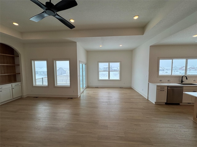 unfurnished living room with a textured ceiling, light wood-type flooring, a sink, and baseboards