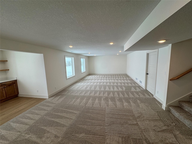 basement featuring visible vents, stairs, baseboards, and a textured ceiling