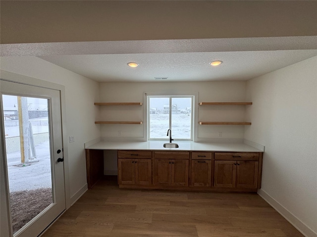 kitchen featuring light wood-style flooring, a sink, visible vents, open shelves, and brown cabinetry