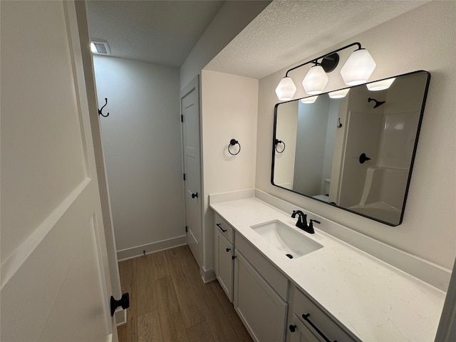 bathroom featuring visible vents, toilet, a textured ceiling, vanity, and wood finished floors